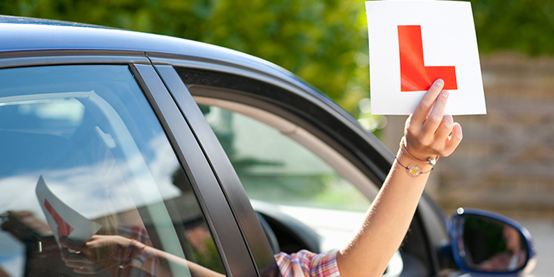 Learner driver holding an L plate out of a car window