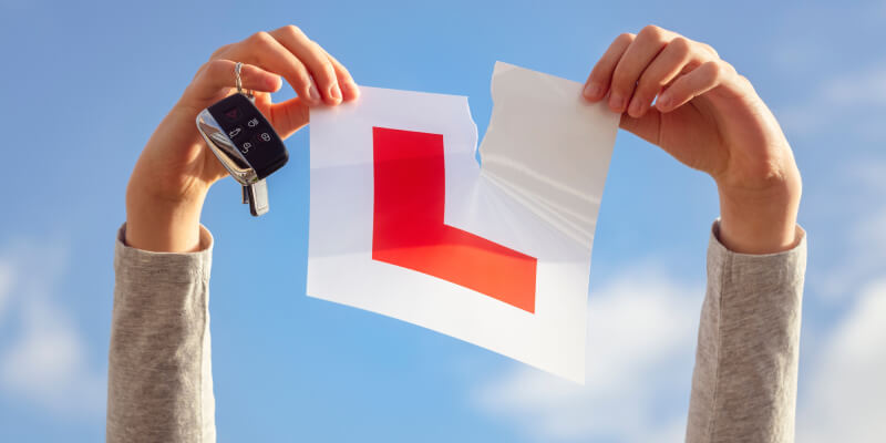Hands in air holding keys and ripping learner sign